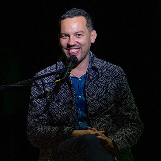 Justin Torres sits on stage with dark background smiling
